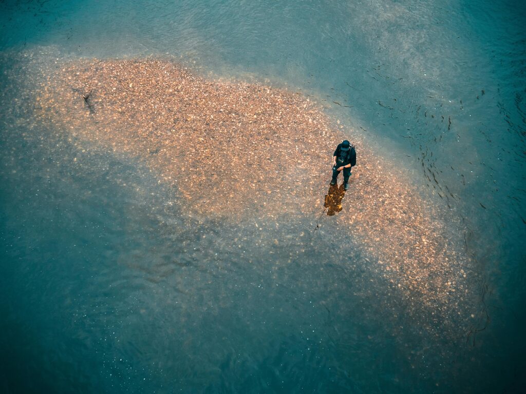 Man fishing in river on rocks. By Jordan Benton